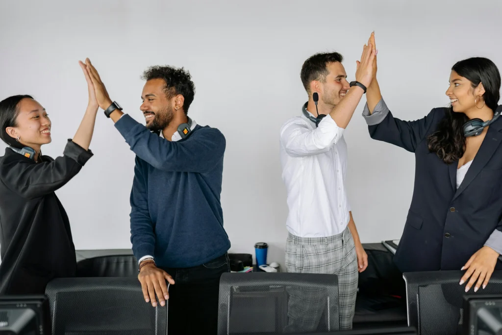 Quatre collègues souriants se faisant des high-fives au bureau, illustration de la cohésion d'équipe en entreprise