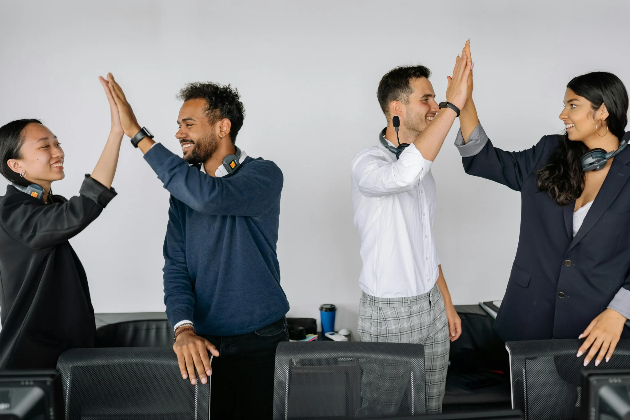 Quatre collègues souriants se faisant des high-fives au bureau, illustration de la cohésion d'équipe en entreprise